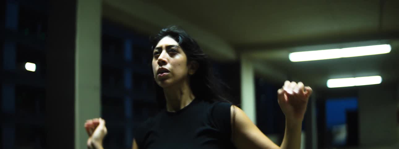 Woman dancing with intense expression in a nighttime urban setting