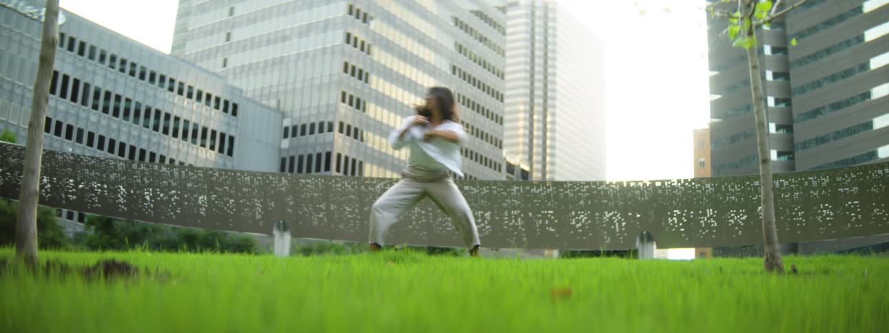 Woman practicing tai chi barefoot in an urban green space