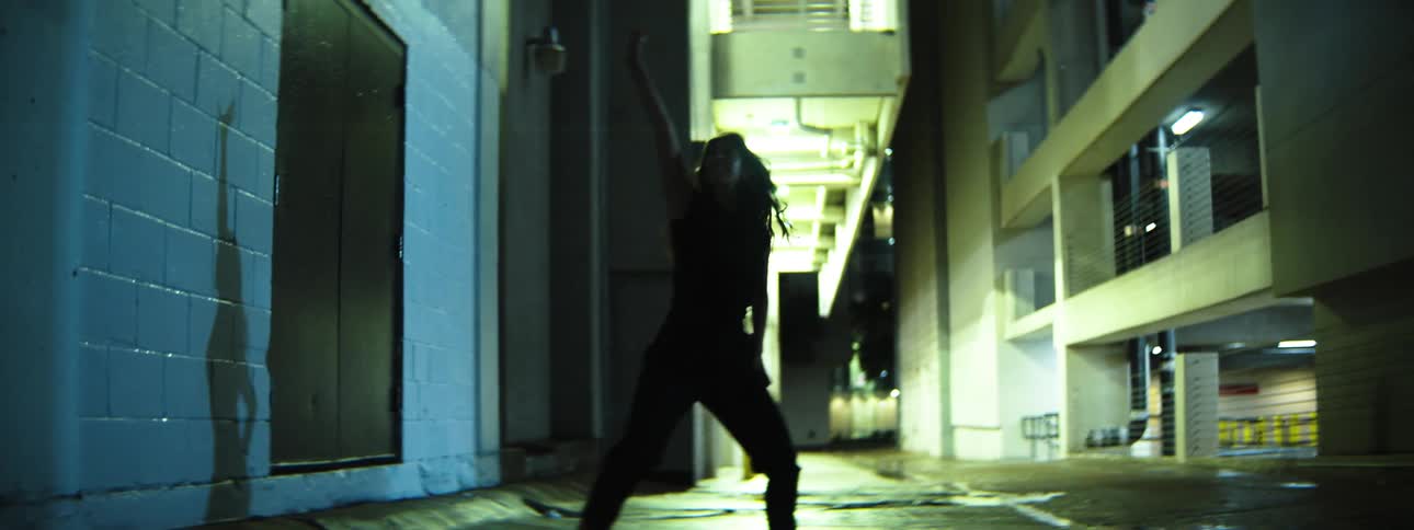 A female dances in a dimly lit alley at night