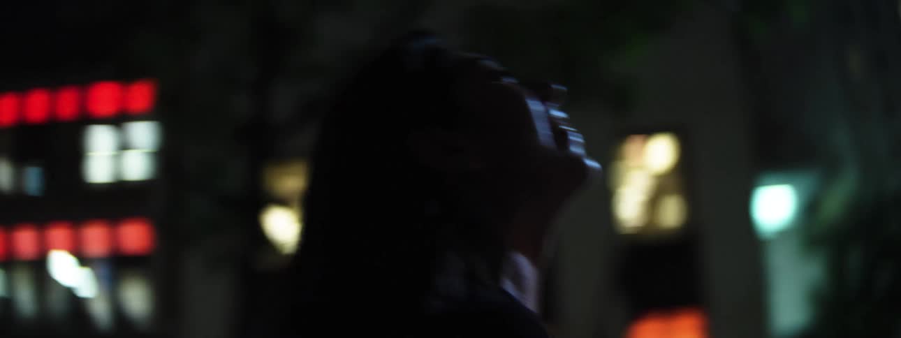 A hispanic woman with long dark hair dances in a busy city environment at night
