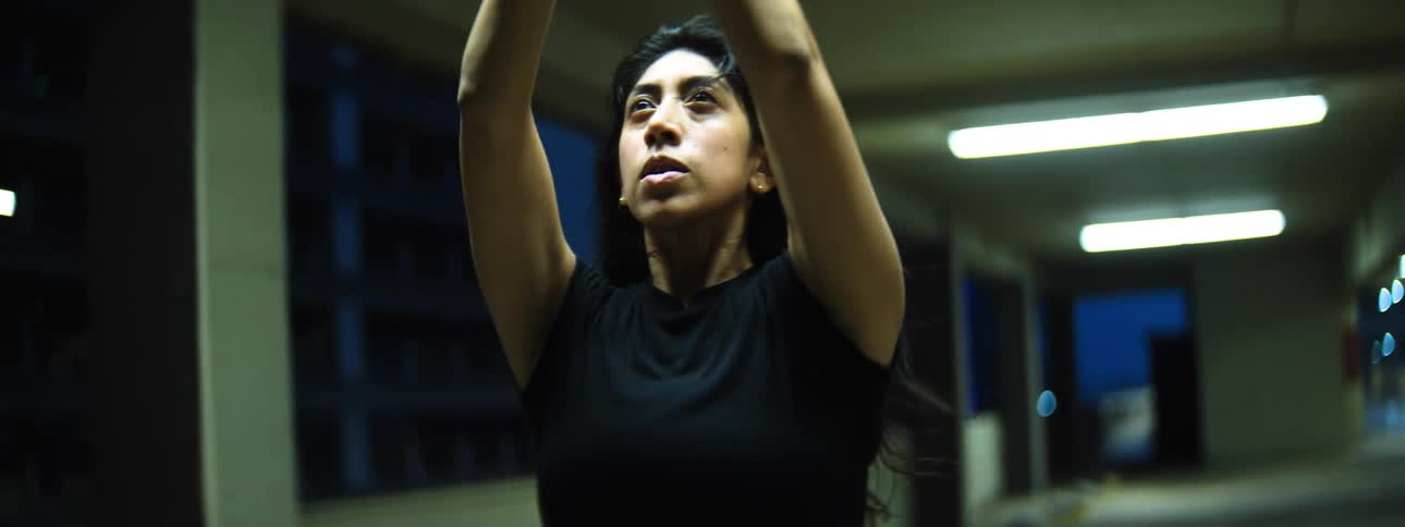 A female standing in a parking garage moves her arms wide backwards and forward