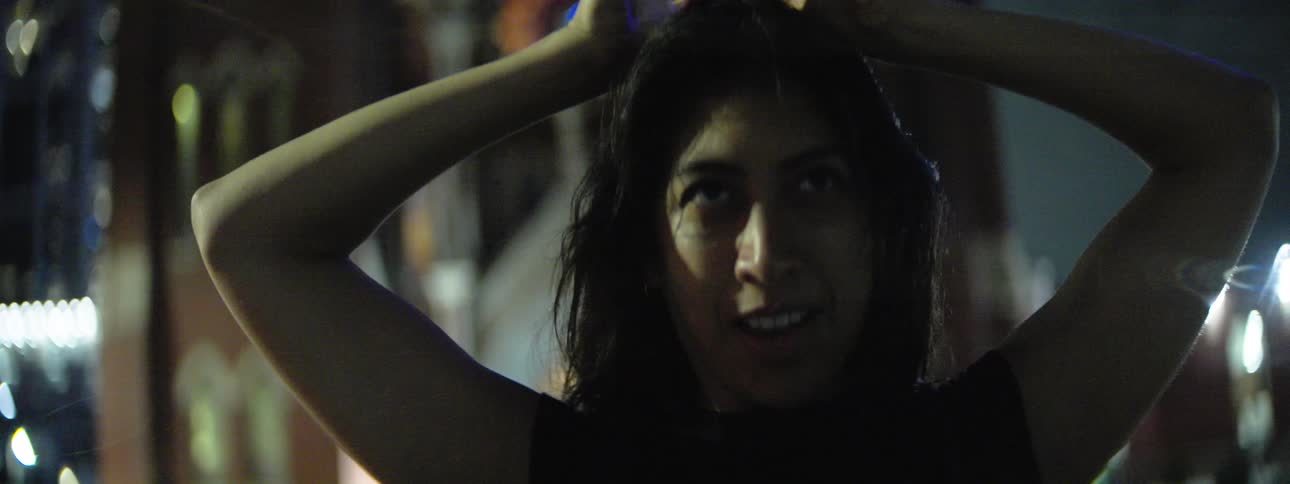 A female is standing in front of a church reaching her arms up and moving them around while smiling