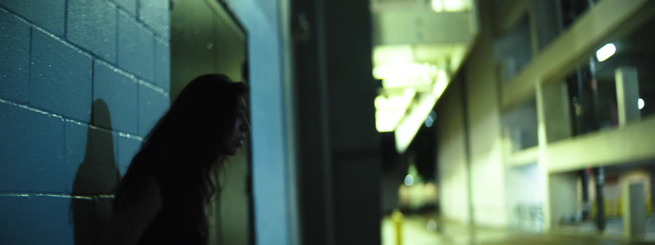 A woman with dark hair backs up and leans against a building at night