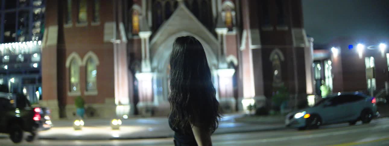 Female gazes up at a glowing church rose window at night posture suggesting awe and quiet reverence