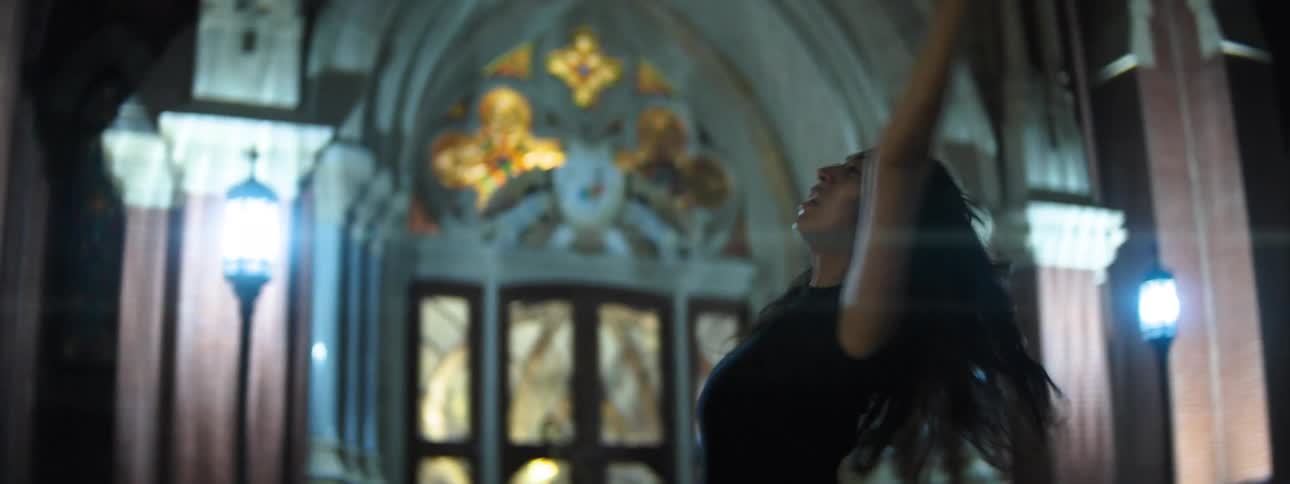A woman holds up her arms and twirls while dancing near a cathedral at night