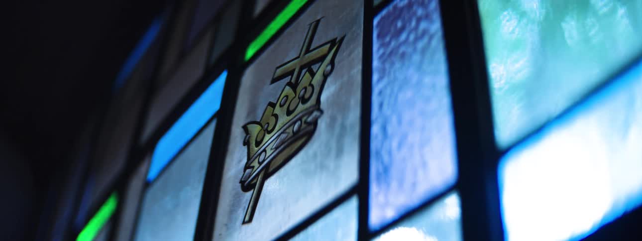 A colorful stained glass window in a cathedral has a crown emblem on it