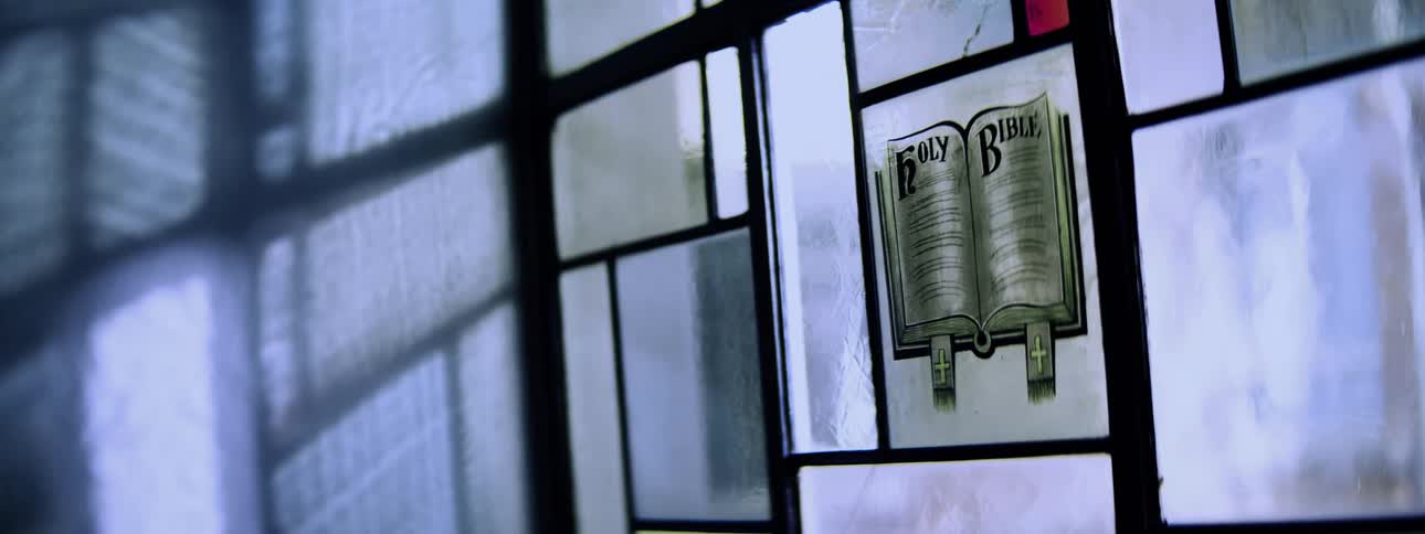 A static closeup shot features a religiousthemed glass panel depicting an open holy bible book with light illuminating the scene
