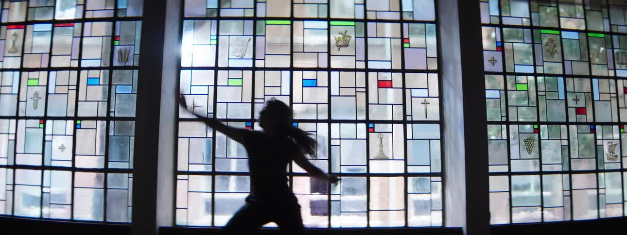 A woman dances in front of a large stained glass window