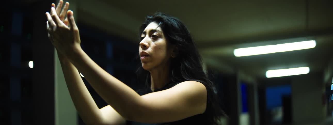 A woman under harsh fluorescent lights moves with her hand raised face glistening and tense looking focused and determineda woman under harsh fluorescent lights moves with her hand raised face glistening and tense looking focused and determined