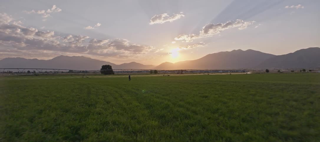 A person walks across a grassy field at sunrise with mountains behind