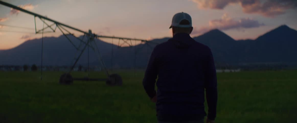 Male farmer walks across a crop field spanned by an irrigation system at dawn