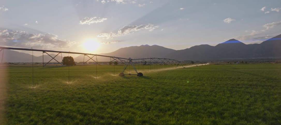 Large scale agricultural irrigation system sprays the crops in a field near the mountains on a cloudy day