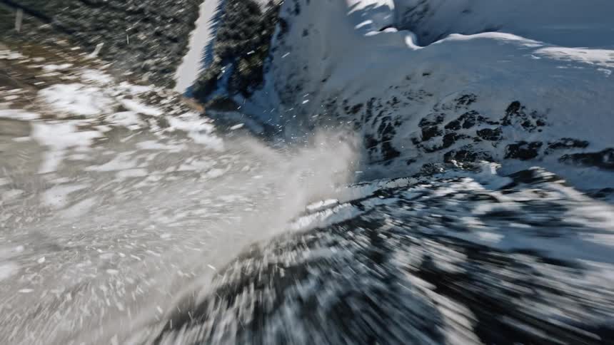 A turn around a snow covered mountain side then as snow pours down a path down the mountain a turn to follow it into a dive