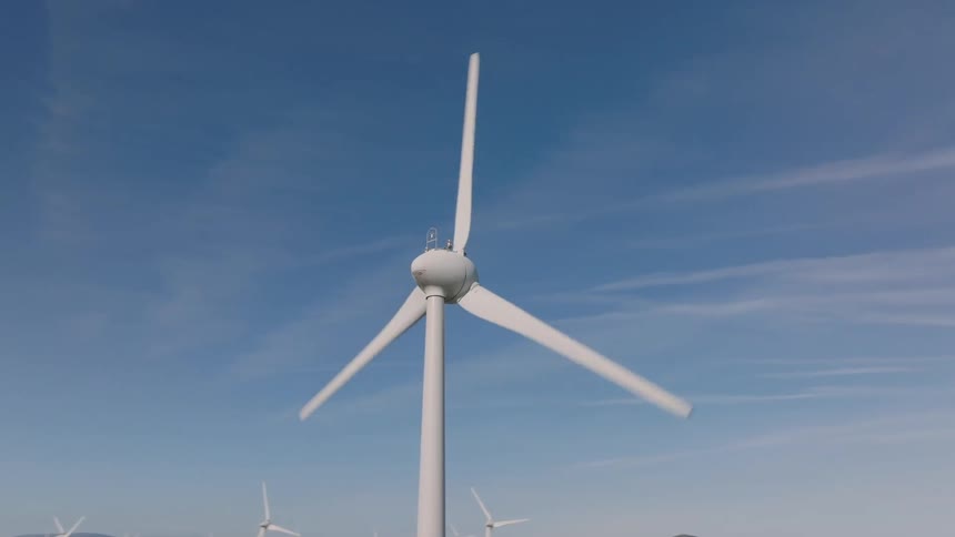 Operating wind turbine standing out against a blue sky with thin clouds