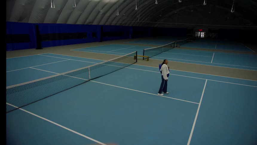 A young black female athlete looking around while standing in a lit indoor tennis court