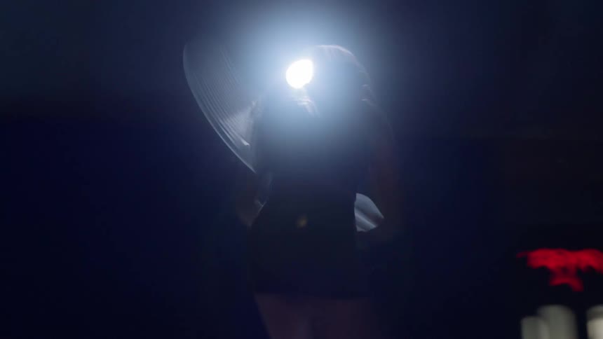 A female tennis player silhouetted against a bright court light practices her swing with intensity