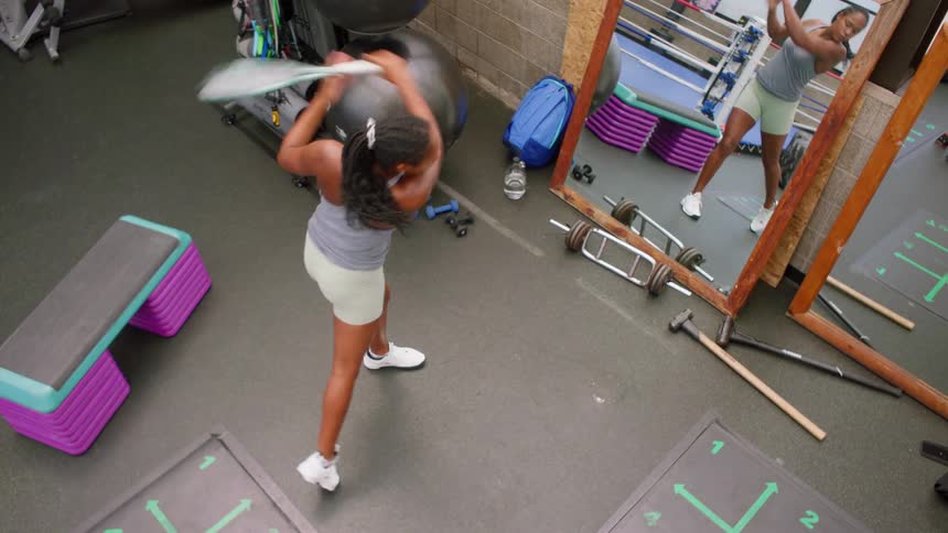 A focused female athlete practices powerful tennis swings with a racket in a gym reflected in a large mirror