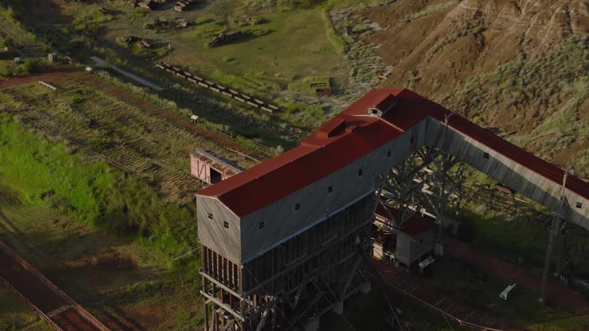 Sunlit aerial view of a weathered industrial conveyor building spanning green rugged terrain