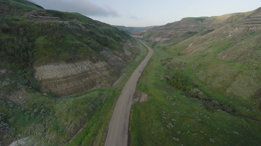 Aerial of a person riding a motorcycle on a road between mountains during daytime