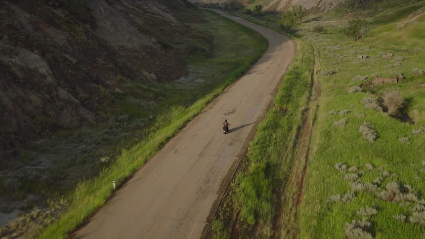 Aerial of a person riding a motorcycle on a road between mountains during daytime