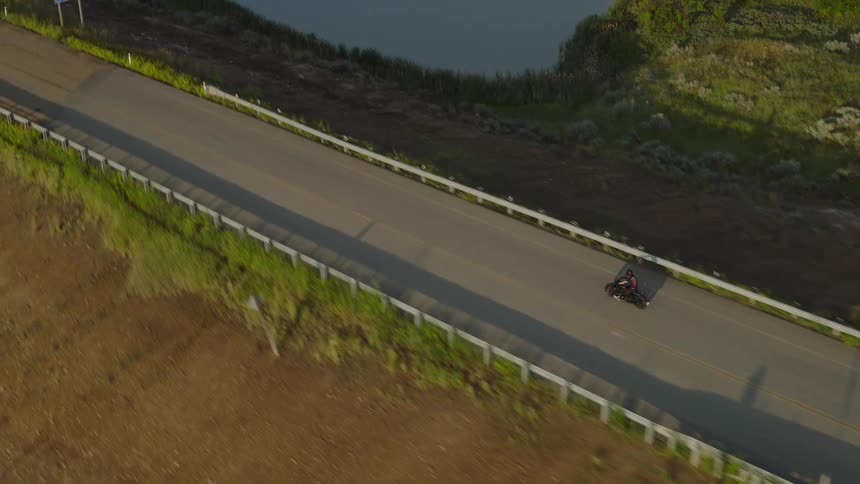 Motorcyclist riding along an asphalt road at sunrise with large shadow