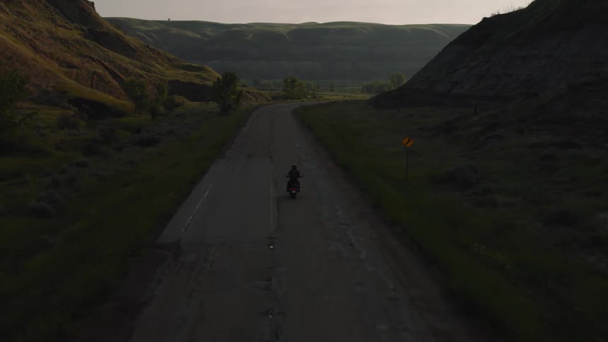 Aerial of a person riding a motorcycle on a road between highlands during daytime