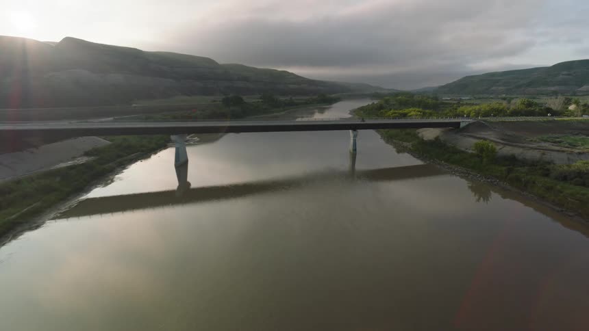 Aerial of a person riding a motorcycle across a bridge that spans over a river during daytime