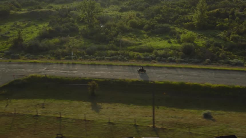Aerial of a person riding a motorcycle on a lonely road in rural area during daytime