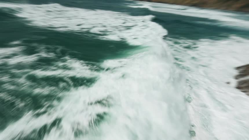 An aerial view of turbulent ocean water and forested coastline visible in the background under a dramatically cloudy sky