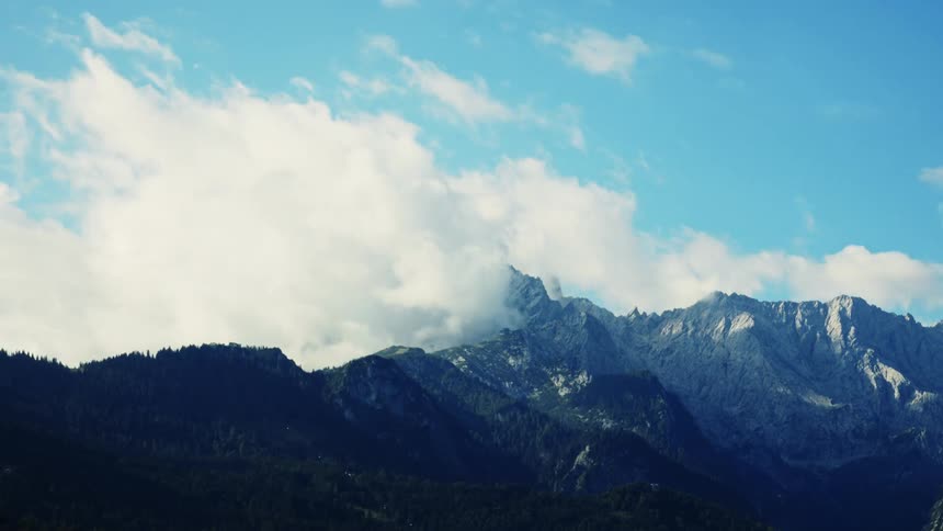Billowing clouds drift across jagged bluegray mountains under a clear sky