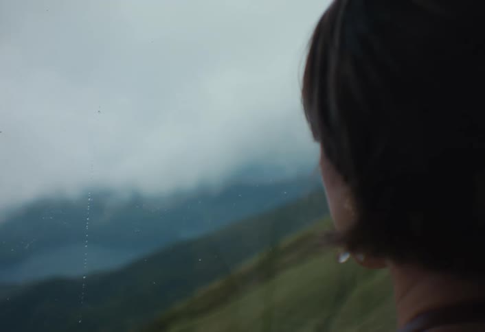 The woman is looking at the mountains from the window