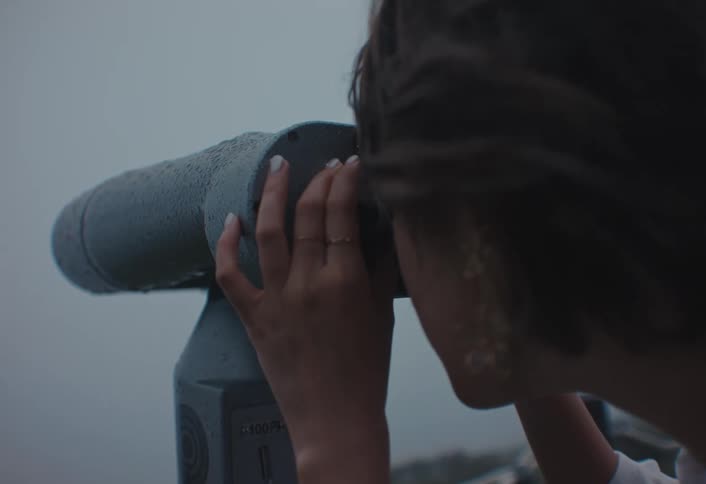 A female looks through binoculars into a distant foggy horizon