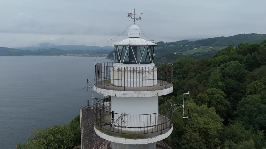 An old lighthouse with a house next to it on top of a mountain peninsula surrounded by trees