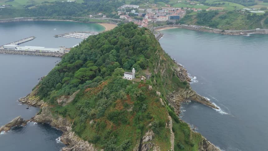 Aerial view of a green island with a lighthouse and small buildings on top