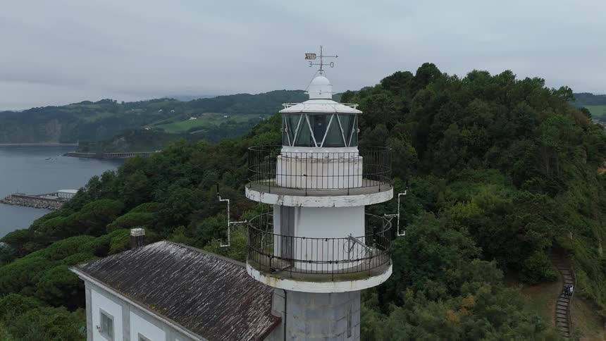 An old lighthouse with a house next to it on top of a mountain peninsula surrounded by trees
