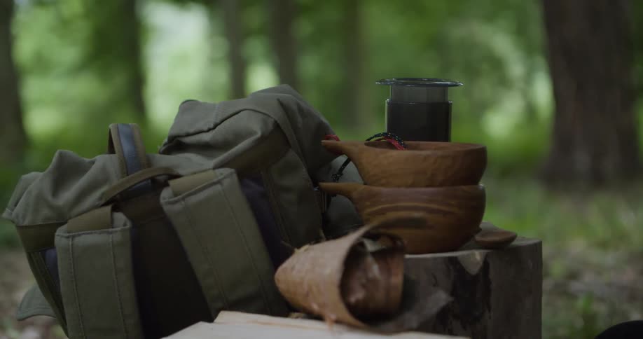 Green backpack beside wooden utensils on a tree stump in the forest
