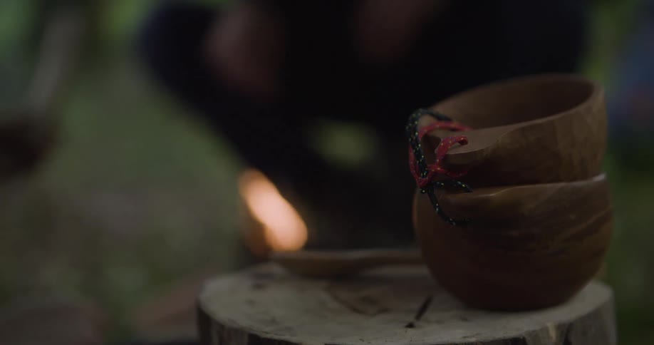 Close up of two wooden bowls and a utensil placed on a tree stump outdoors during daytime