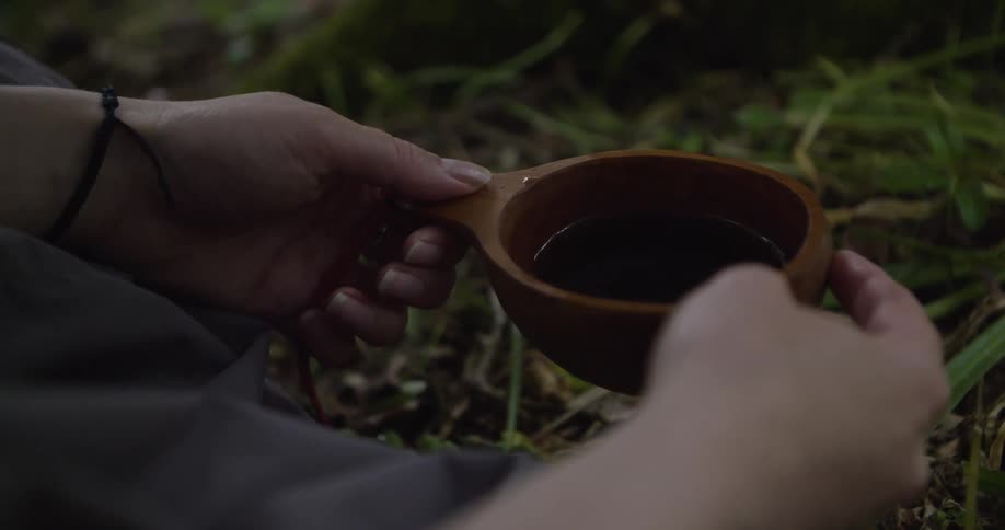 The person is holding a drink in a wooden cup