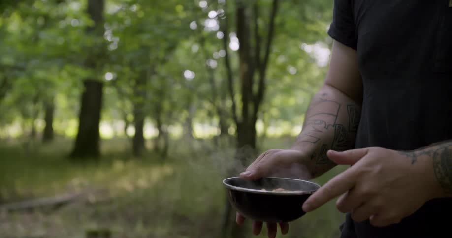 Close up of a woman handing a bowl of food over to a man standing outdoors in a woodland area during daytime