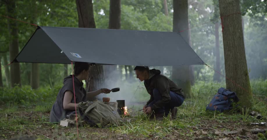 The man and woman cook together under the tent of the camp site