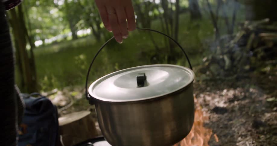 The woman carries the pot to the campfire