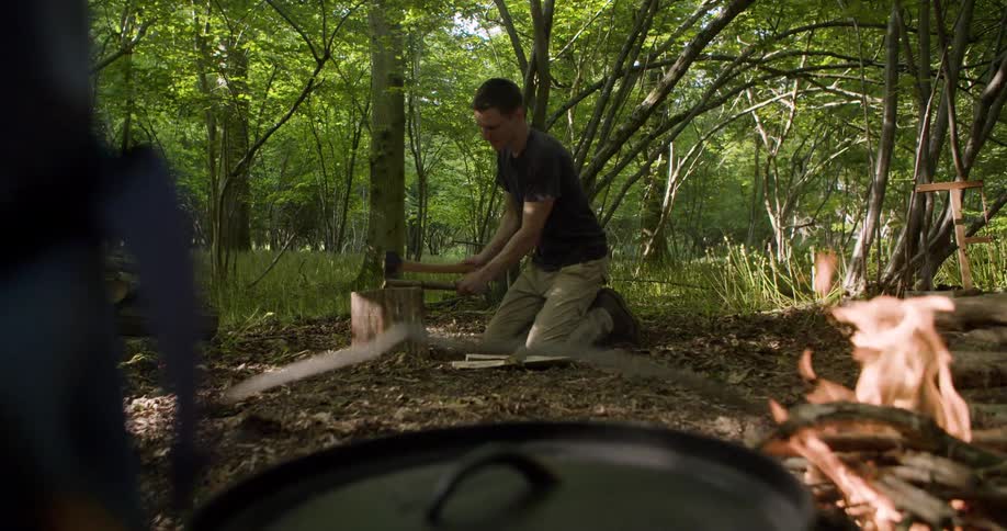 A man splits wood in the forest at midday stacking the pieces to create a bonfire surrounded by trees