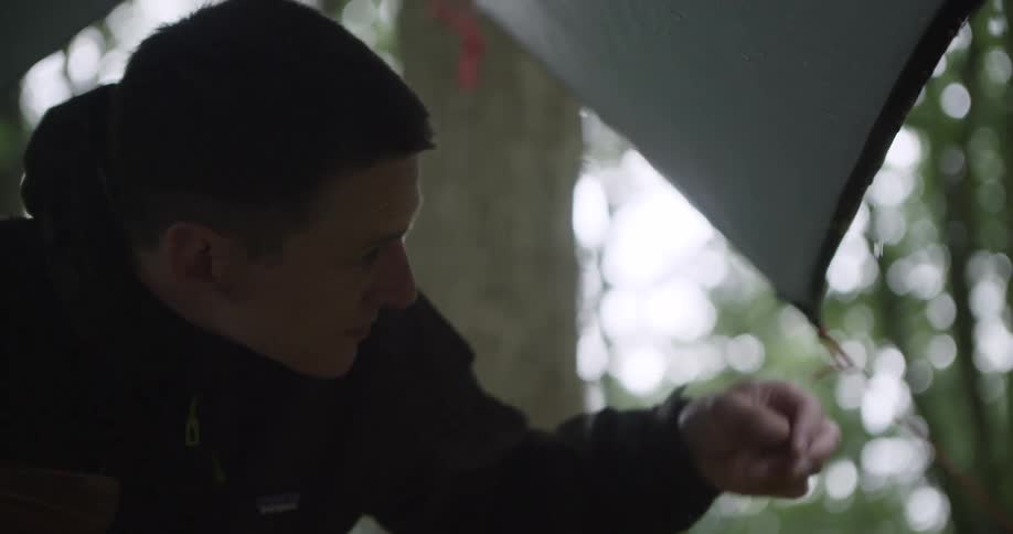 The man sits under a tent as it rains in the forest