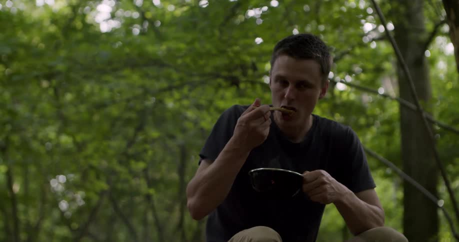 The man eats with a wooden spoon at the camp site