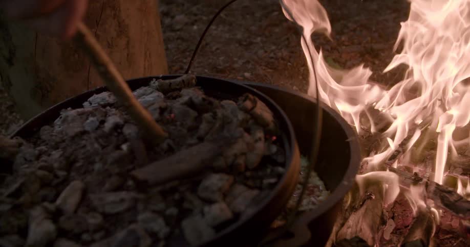 The person is cooking a pot of food on the campfire