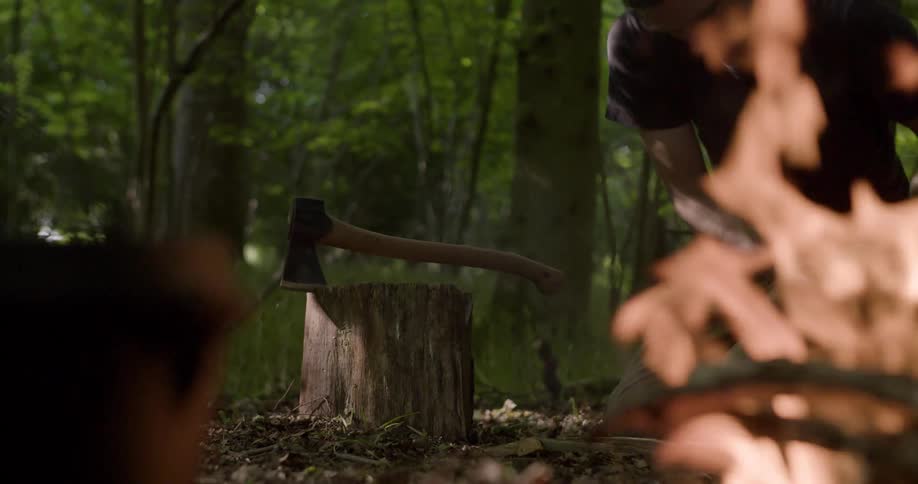The man gathers sticks to put in the campfire