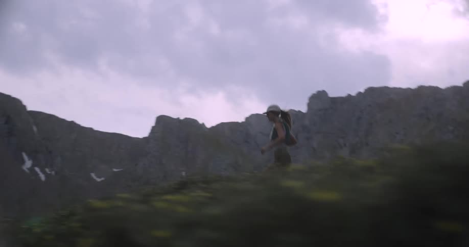 The woman is running through the bushes by the mountains