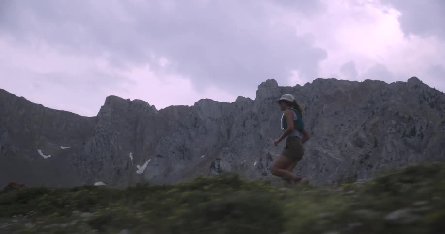 A young woman running across a rocky grass field outdoors during daytime