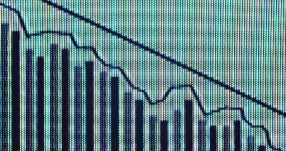 Extreme macro view of a digital screen with RGB pixels shows a black line graph with a downward pointing arrow overlaying vertical black bar charts representing a stock market crash or economic downturn with negative trend