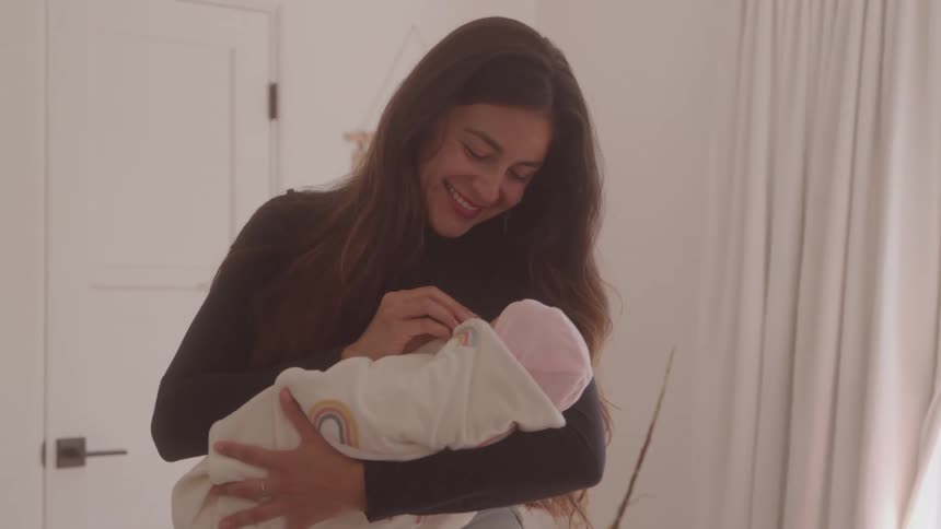 Woman holding a baby wrapped in a white blanket with rainbow patterns